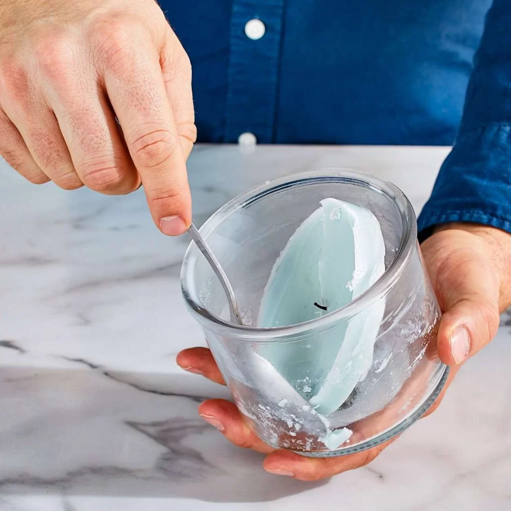 Man Scooping Wax Out Of Glass Candle Jar